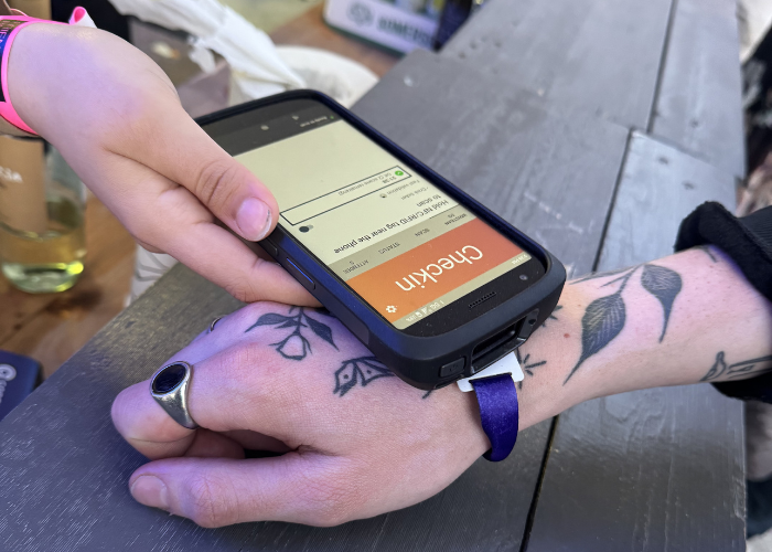A handheld scanner reading a woven purple wristband with an RFID chip at a food stall.