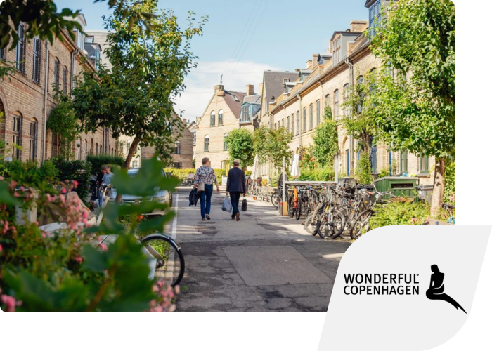A street with flats, green plants and bicycles on both sides. The Wonderful Copenhagen logo is inset in the corner.